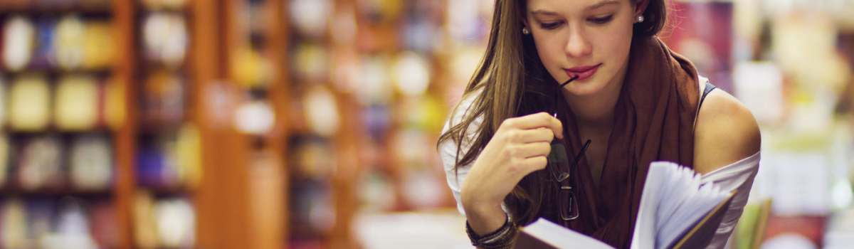 mujer joven leyendo un libro en una biblioteca, estudiando